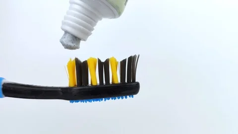 Blue toothpaste with carbon specks is gently squeezed out of the tube onto a dar Stock Footage 125084533