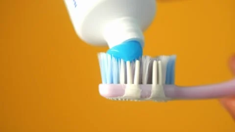 Blue toothpaste squeezed onto purple toothbrush over yellow background in s.. Vídeos de archivo 332784898