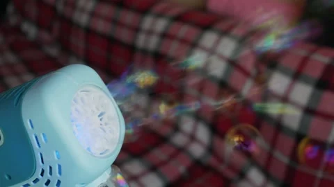 Blue Toy Bubble Machine Blowing Bubbles Against Plaid Blanket Background Stock Footage 339176977