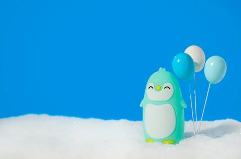 Blue toy penguin with balloons on the snow with copy space. Stock Photos