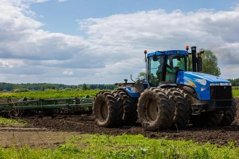 Blue tractor with double wheels pulling disc harrow with roller basket at hot Stock Photos