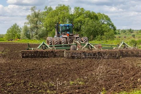 Blue tractor with double wheels pulling disc harrow with roller basket at hot Stock Photos