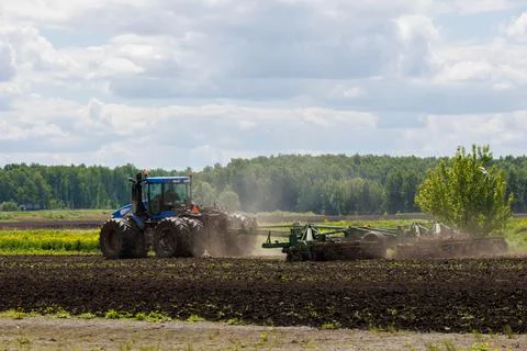Blue tractor with double wheels pulling disc harrow with roller basket at hot Stock Photos