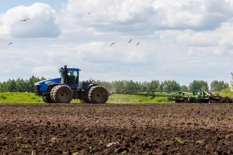 Blue tractor with double wheels pulling disc harrow with roller basket at hot Photos
