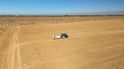 A blue tractor is driving through a plantation field and pulling irrigation equi Stock Footage 335874674