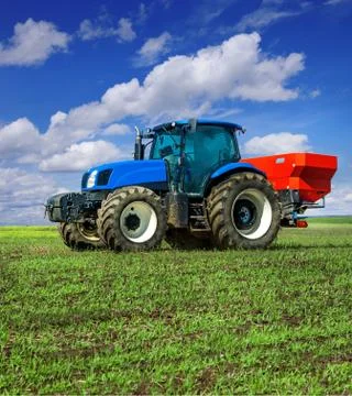 Blue tractor in field work with modern red two-disc fertiliser spreader spray Stock Photos