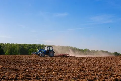 Blue tractor plowing field in spring Stock Photos