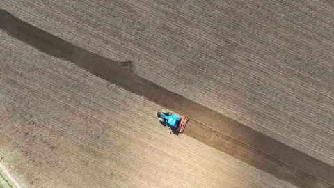 Blue tractor plowing a vast field in diagonal lines, captured from a drone Stock Footage 306653652