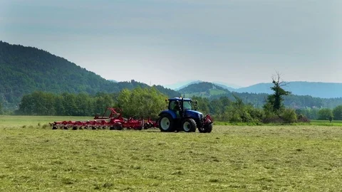 Blue tractor is preparing hay on a large grass field Stock Footage 72377939