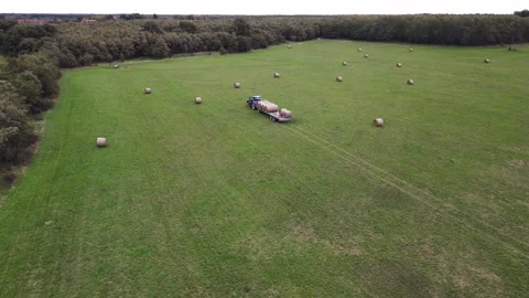 A blue tractor is pulling a fully loaded trailer of round hay bales across Stock Footage 287706306