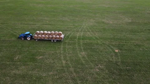 A blue tractor is pulling a fully loaded trailer of round hay bales across Stock Footage 287706337
