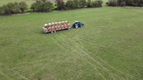 A blue tractor is pulling a fully loaded trailer of round hay bales across Stock Footage 287706601