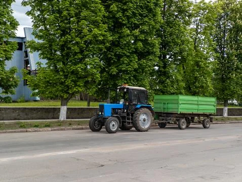 A blue tractor pulling a green trailer down a street Stock Photos