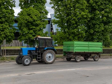 A blue tractor pulling a green trailer down a street Stock-Fotos