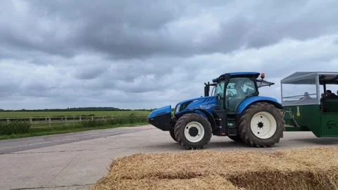 Blue tractor pulling a passenger trailer through a rural landscape Vídeos de archivo 337356793