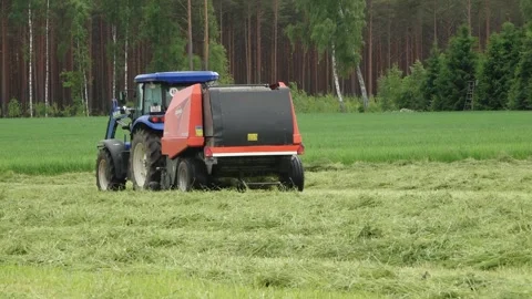 Blue tractor pulls a round baler producing a fresh hay bale in a rural field Video stock 337256883