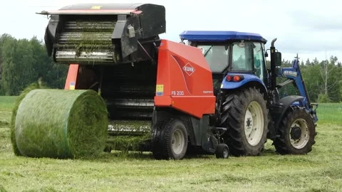 Blue tractor pulls a round baler producing a fresh hay bale in a rural field Video stock 337256888
