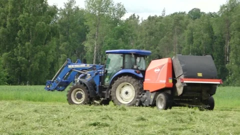 Blue tractor pulls a round baler producing a fresh hay bale in a rural field Video stock 337256903