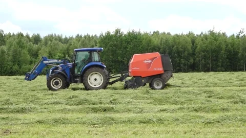 Blue tractor pulls a round baler producing a fresh hay bale in a rural field Video stock 337256956