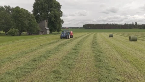 Blue tractor pulls a round baler producing a fresh hay bale in a rural field Video stock 337257269