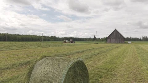 Blue tractor pulls a round baler producing a fresh hay bale in a rural field Video stock 337257341