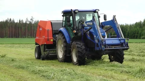 Blue tractor pulls a round baler producing a fresh hay bale in a rural field Video stock 337741117