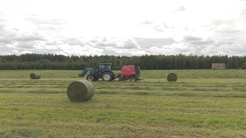 Blue tractor pulls a round baler producing a fresh hay bale in a rural field. Video stock 337741639