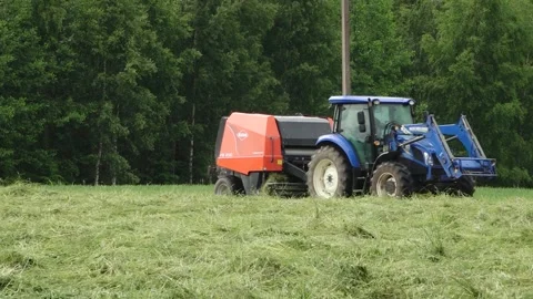 Blue tractor pulls a round baler producing a fresh hay bale in a rural field Video stock 337742031