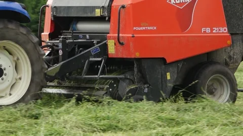 Blue tractor pulls a round baler producing a fresh hay bale in a rural field Video stock 337950781