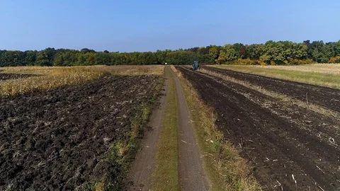 A blue tractor sitting in the middle of a plowed filed, filmed with a drone. Stock Footage 113101125