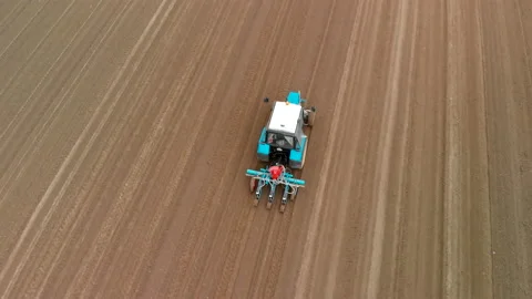 A blue tractor works in the spring against the background of a huge brown field Vídeos de archivo 132150292