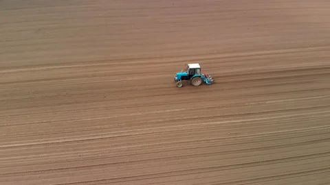 A blue tractor works in the spring against the background of a huge brown field 스톡 동영상 132692633