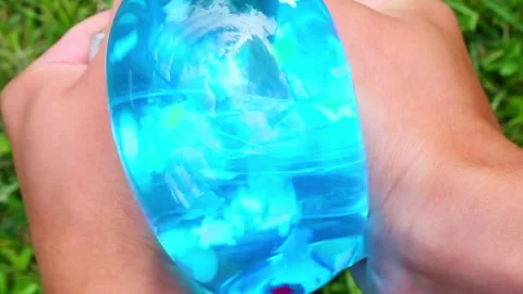 Blue translucent water ball squeezed tightly in hand outdoors Видео 319172201