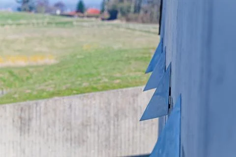 Blue triangular metal vents on building wall with blurred green field backg.. Stock Photos