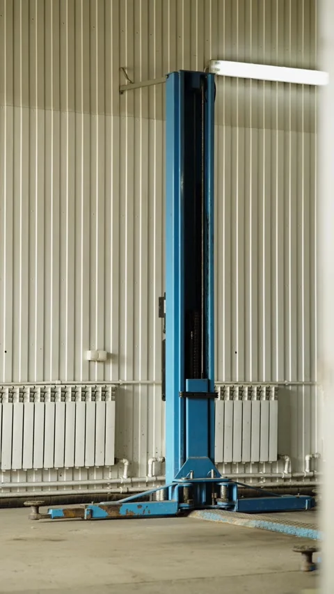 A blue two-post car lift column standing inside an auto repair shop Stock Footage 337890088