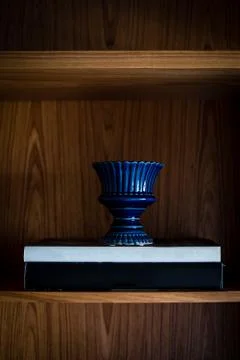 Blue vase on top of two large nondescript book, all in dark shelf, natural si Stock Photos