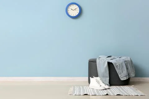 Blue wall with a clock, ottoman, denim jacket, and white sneakers on a stripe Stock Photos