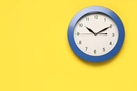 Blue wall clock on yellow background showing 10:10 Stock Photos