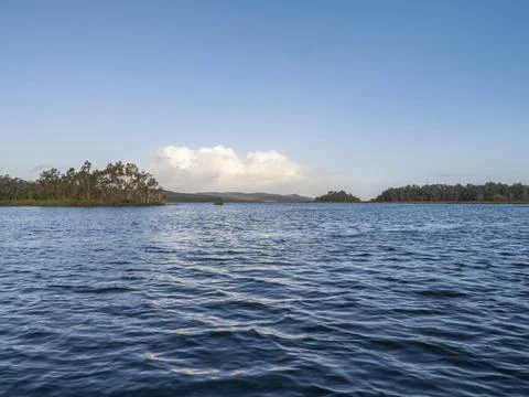 Blue water with distant tree-covered islands under clear sky Stock Photos