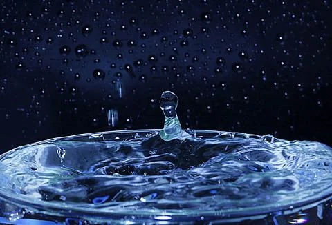 Blue water drops splashed, overflowing the glass. Stock Photos