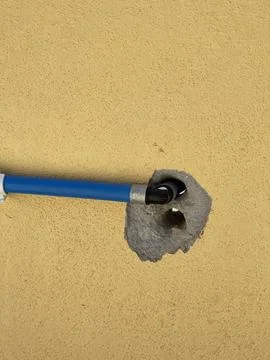 Blue Water Pipe Passing Through Drilled Hole On Yellow Wall Stock Photos
