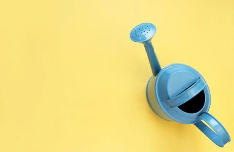 Blue watering can on yellow background. Creative concept of investment, growt Stock Photos