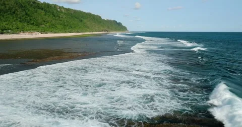 Blue wave crashes on the sandy beach with jungle in Bali Stock Footage 274736842