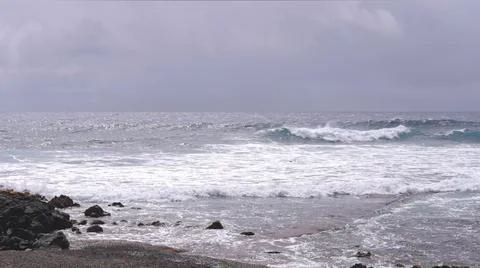 The blue waves of the Pacific Ocean roll over the rocky beach of the Hawaiian Stock Photos