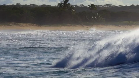 Blue waves roll into the coast of Hawaii and break on the shore. 스톡 동영상 75694553