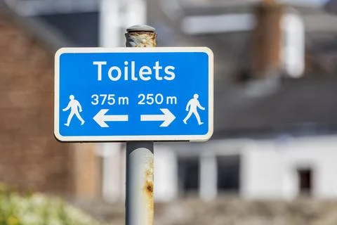 Blue white rectangular sign to nearest public toilets with black text Stock Photos