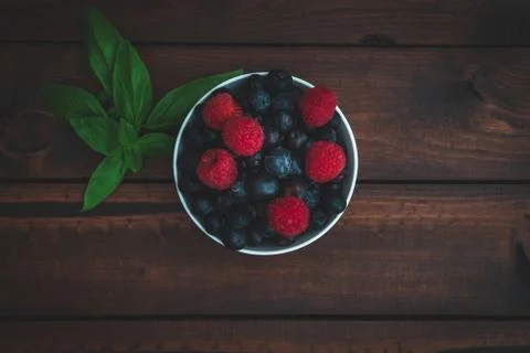 Blueberries and raspberries in a bowl on a dark brown table. Stock Photos