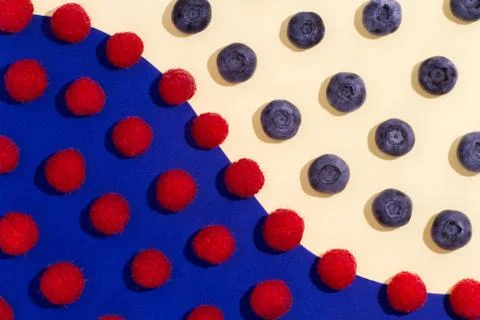 Blueberries and raspberry spaced on a double paper yellow-blue background. Stock Photos