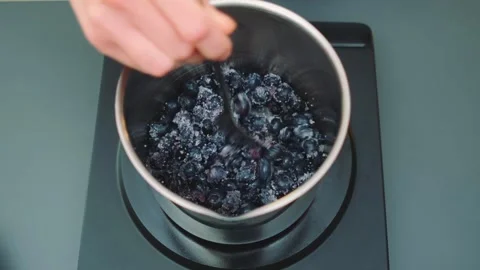 Blueberries and sugar melting while stirring on indoor kitchen stove 库存影片 342883109