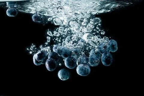 Blueberries splashing in water on black Stock Photos